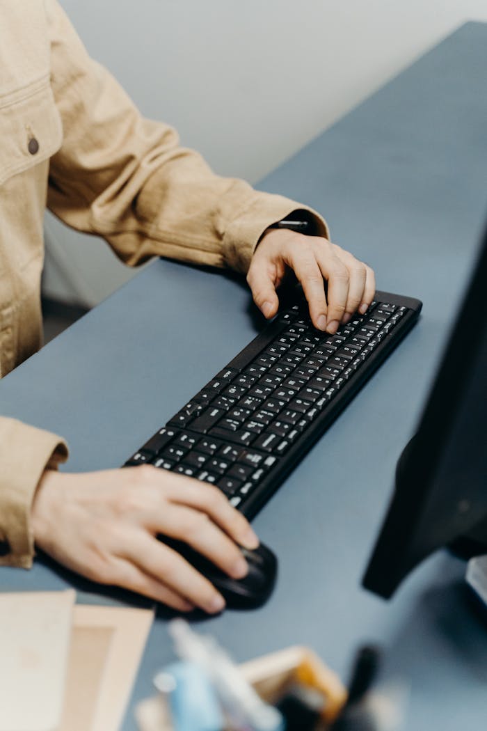 Close-up view of hands typing on a keyboard in an office setting, showcasing productivity at work.